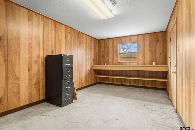 interior space with unfinished concrete flooring, elevator, wood walls, and baseboards