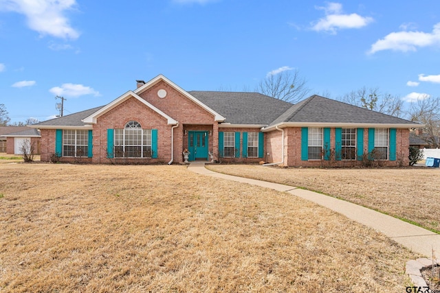 ranch-style house with roof with shingles, brick siding, a chimney, and a front lawn