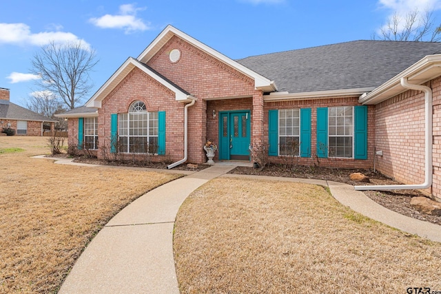 ranch-style house with a front lawn, roof with shingles, and brick siding