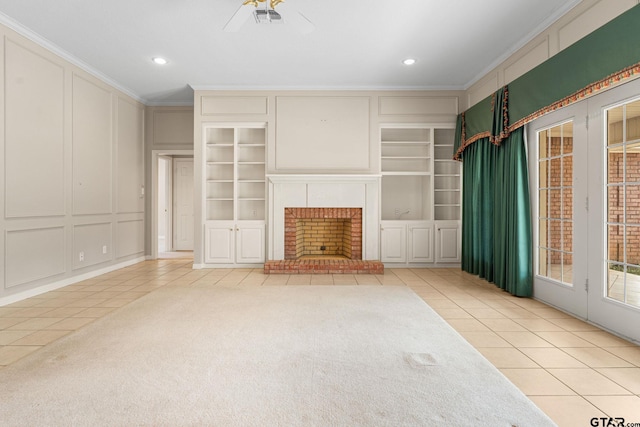 unfurnished living room with built in shelves, carpet floors, crown molding, a decorative wall, and a brick fireplace