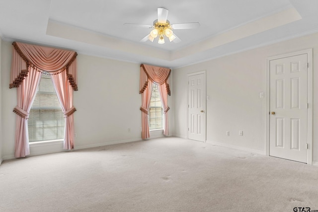 carpeted empty room with a tray ceiling, crown molding, baseboards, and ceiling fan