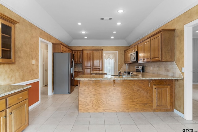 kitchen featuring light stone counters, stainless steel appliances, a peninsula, visible vents, and brown cabinetry