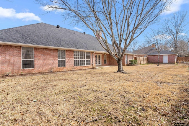 rear view of property with brick siding, fence, a yard, french doors, and roof with shingles