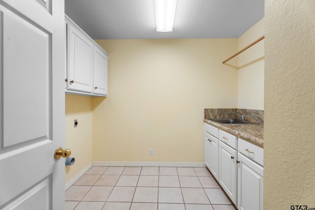 washroom with cabinet space, light tile patterned floors, a textured ceiling, hookup for an electric dryer, and a sink