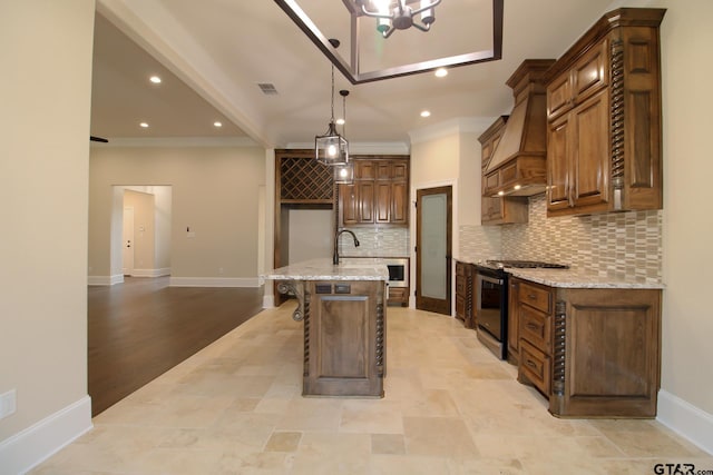 kitchen with a center island with sink, hanging light fixtures, tasteful backsplash, range with gas cooktop, and premium range hood