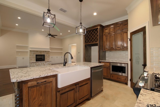 kitchen with a stone fireplace, sink, an island with sink, appliances with stainless steel finishes, and decorative light fixtures