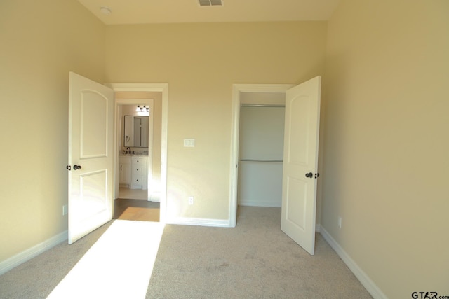 unfurnished bedroom with ensuite bathroom and light carpet