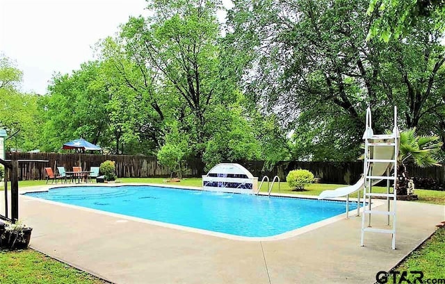 view of swimming pool featuring a fenced in pool, a fenced backyard, a water slide, a yard, and a patio area