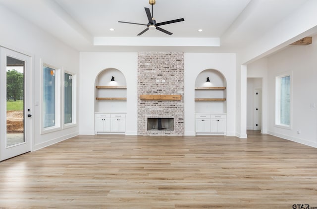 unfurnished living room featuring a brick fireplace, built in features, light hardwood / wood-style flooring, and a tray ceiling