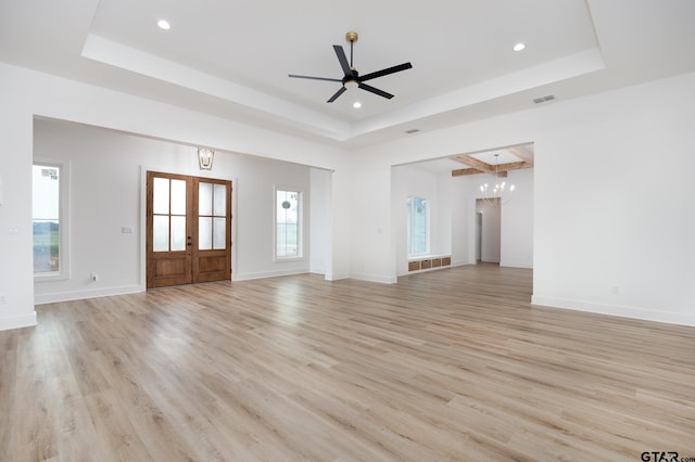 unfurnished living room with french doors, ceiling fan with notable chandelier, light hardwood / wood-style flooring, and a raised ceiling