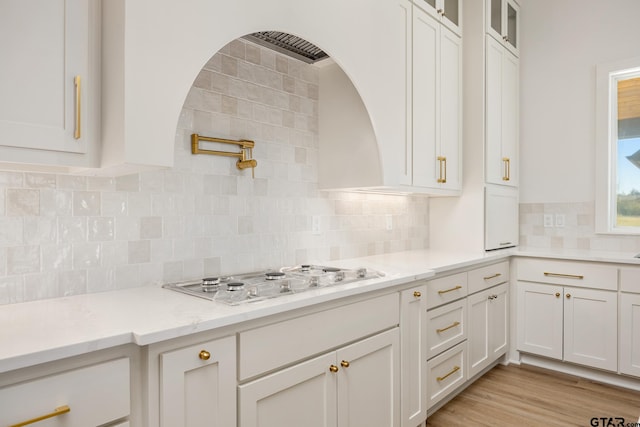 kitchen featuring white gas stovetop, backsplash, light stone countertops, white cabinets, and light hardwood / wood-style flooring