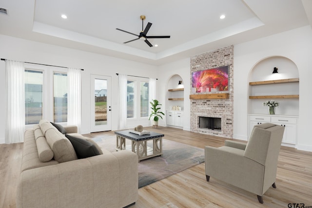 living room with a fireplace, built in features, light wood-type flooring, and a tray ceiling