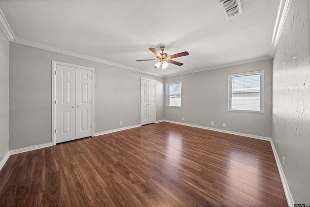 unfurnished bedroom with two closets, crown molding, visible vents, and wood finished floors