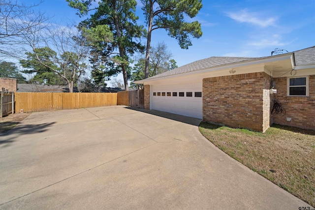 view of side of home with an attached garage, driveway, fence, and brick siding