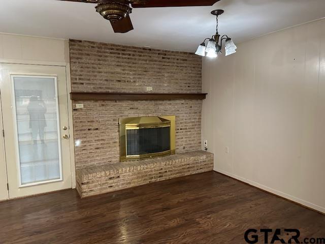 504 Mt Sylvan, Lindale, TX 75771 - unfurnished living room featuring dark wood-type flooring, ceiling fan, a chandelier, a brick fireplace, and baseboards
