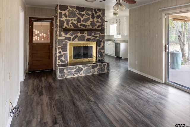 unfurnished living room with a ceiling fan, a sink, a stone fireplace, crown molding, and dark wood-style flooring