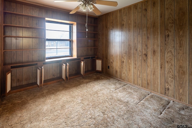 carpeted spare room featuring wooden walls and ceiling fan