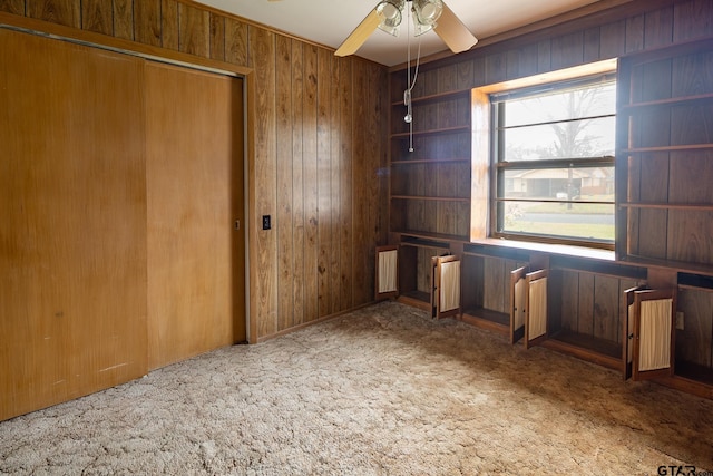 interior space featuring a closet, a ceiling fan, wood walls, and carpet flooring