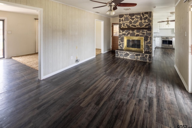 unfurnished living room with a stone fireplace, dark wood-style floors, visible vents, and ceiling fan