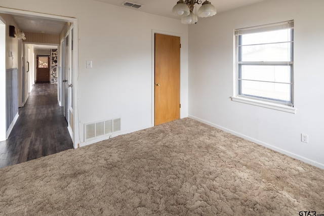 spare room with a chandelier, visible vents, baseboards, and dark colored carpet