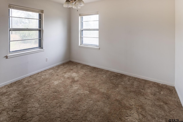 empty room with a chandelier, baseboards, and carpet