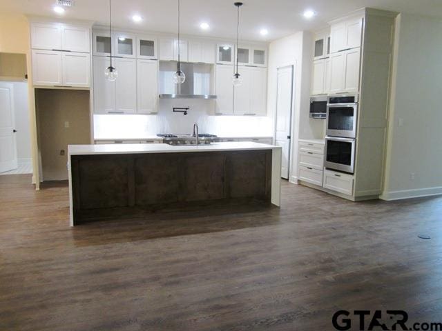 kitchen with dark hardwood / wood-style flooring, stainless steel double oven, white cabinets, and a kitchen island with sink