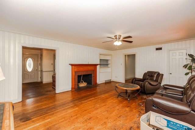 living room featuring ceiling fan, crown molding, wood-type flooring, and a brick fireplace