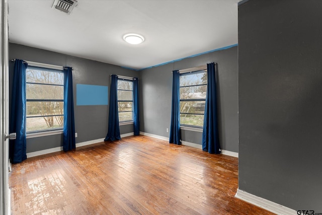 unfurnished room with baseboards, visible vents, and hardwood / wood-style floors