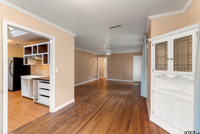 empty room featuring ceiling fan, wood finished floors, visible vents, and crown molding