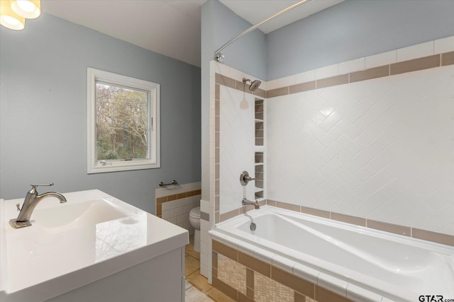 bathroom featuring tiled shower / bath, vanity, and toilet