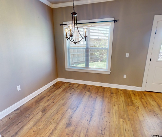 unfurnished dining area featuring crown molding, baseboards, an inviting chandelier, and wood finished floors