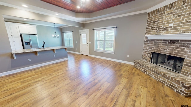 unfurnished living room featuring a tray ceiling, a sink, a brick fireplace, light wood finished floors, and baseboards
