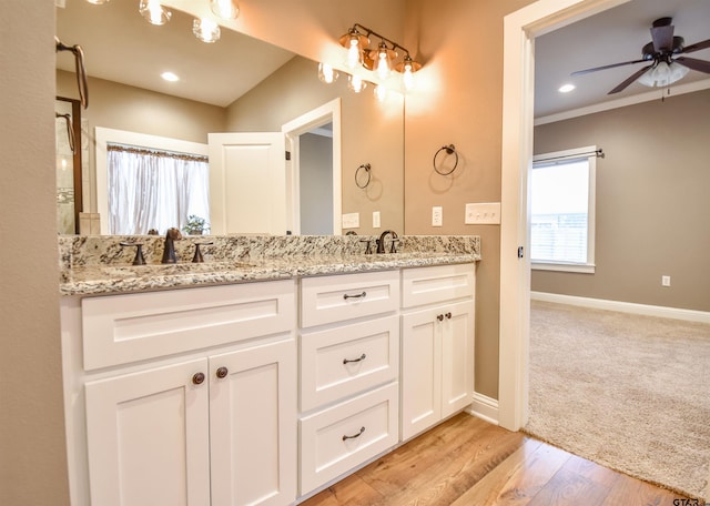 bathroom with a ceiling fan, wood finished floors, a sink, double vanity, and baseboards