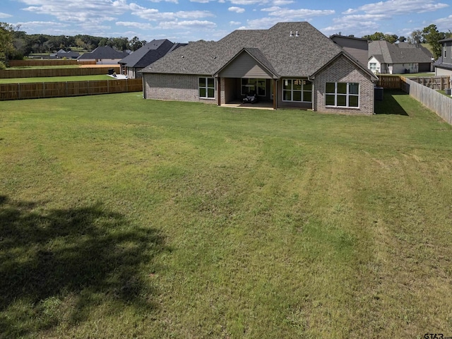 rear view of house with a fenced backyard, roof with shingles, a lawn, and brick siding