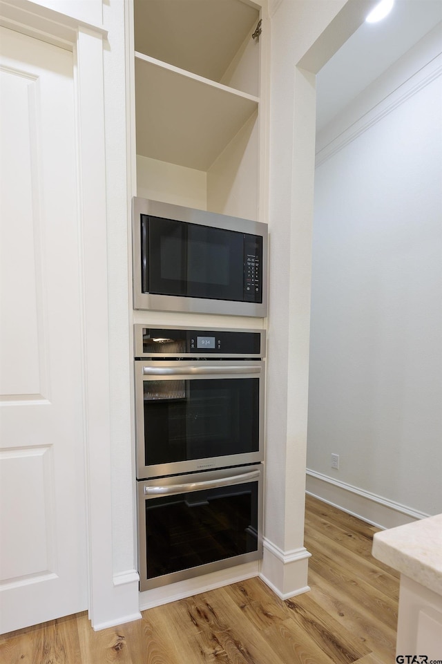 kitchen with light wood-style floors, double oven, built in microwave, and baseboards