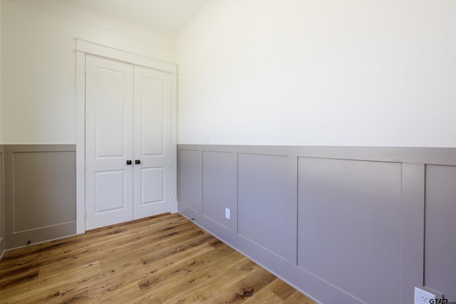 unfurnished bedroom with crown molding, wainscoting, light wood-type flooring, and a decorative wall