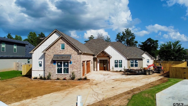 modern farmhouse style home with brick siding, a shingled roof, board and batten siding, fence, and driveway