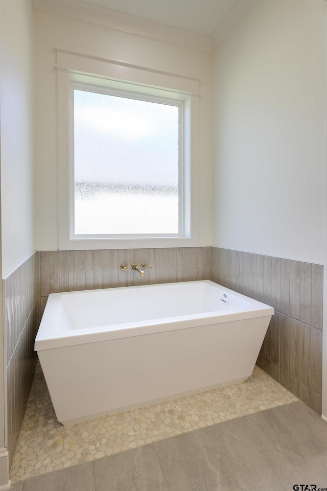 bathroom with wainscoting, a freestanding tub, and tile walls