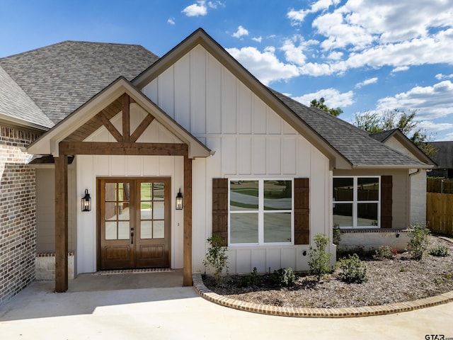 property entrance featuring roof with shingles, french doors, board and batten siding, and brick siding