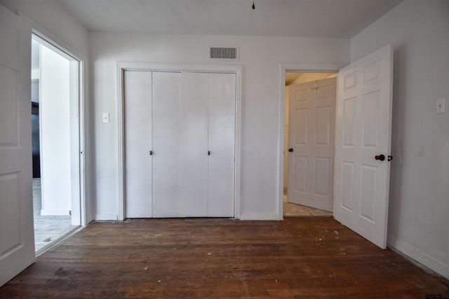 unfurnished bedroom with baseboards, visible vents, dark wood finished floors, and a closet