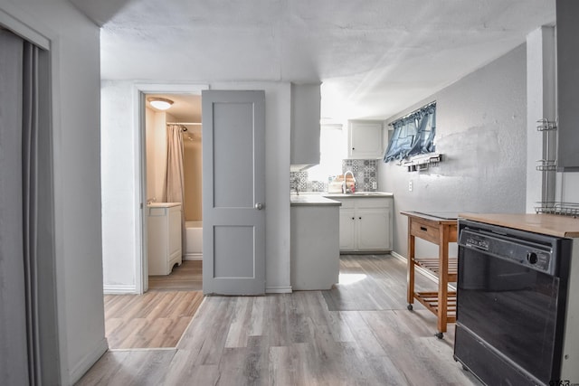 kitchen featuring a sink, baseboards, light wood-style floors, light countertops, and dishwasher