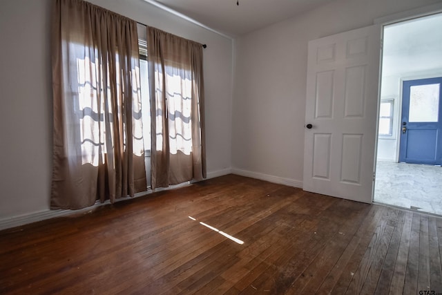 spare room featuring baseboards and dark wood-type flooring