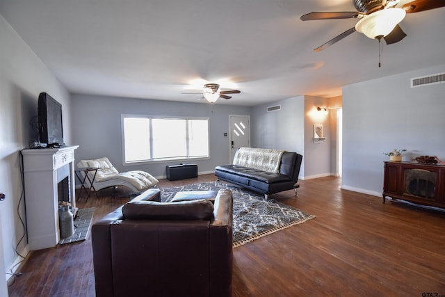 living area featuring dark wood-style floors, a fireplace with raised hearth, visible vents, and a ceiling fan