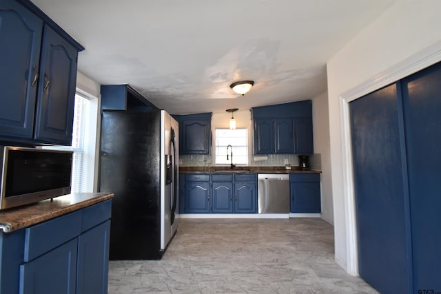 kitchen with dark countertops, blue cabinets, a sink, stainless steel appliances, and backsplash