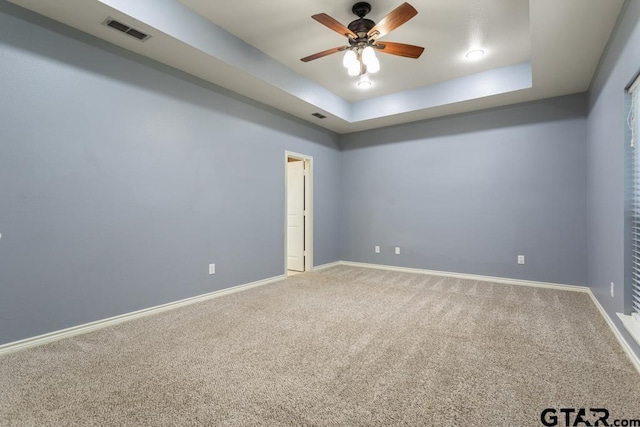 carpeted empty room featuring ceiling fan and a raised ceiling