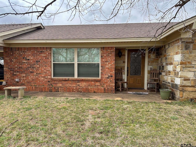 entrance to property with a yard, stone siding, brick siding, and roof with shingles