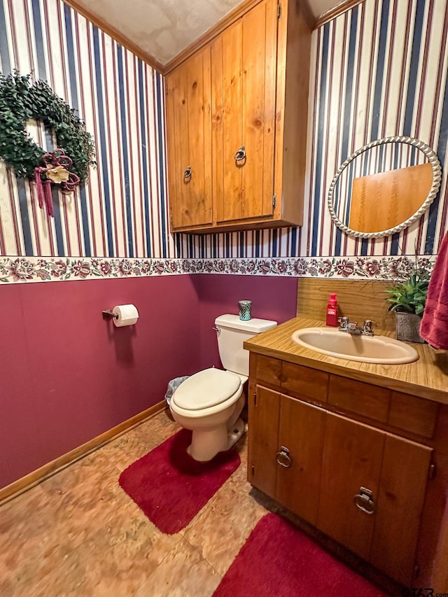 half bathroom with wallpapered walls, toilet, vanity, and baseboards