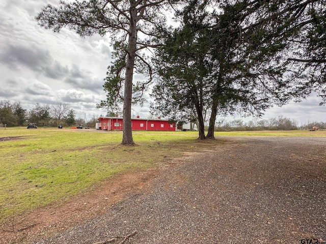 view of front facade featuring an outbuilding, a pole building, a front lawn, dirt driveway, and a detached garage