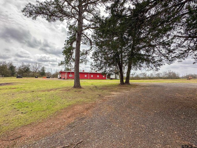 view of front facade featuring an outbuilding, a pole building, a front lawn, dirt driveway, and a detached garage