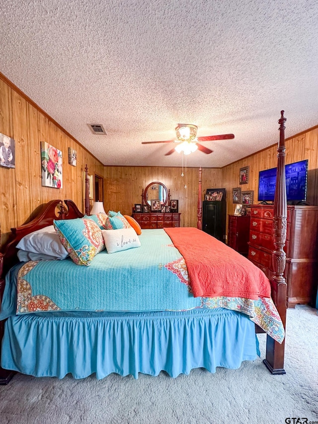 carpeted bedroom with visible vents, ceiling fan, a textured ceiling, and wooden walls